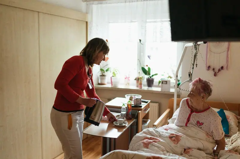 A caregiver bringing tea to an older woman resting in bed