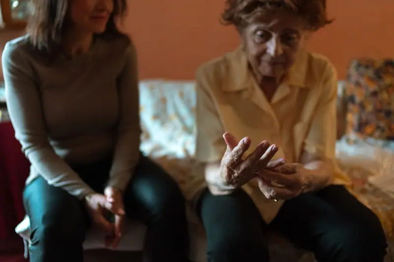 An older woman and her caregiver talking on the sofa