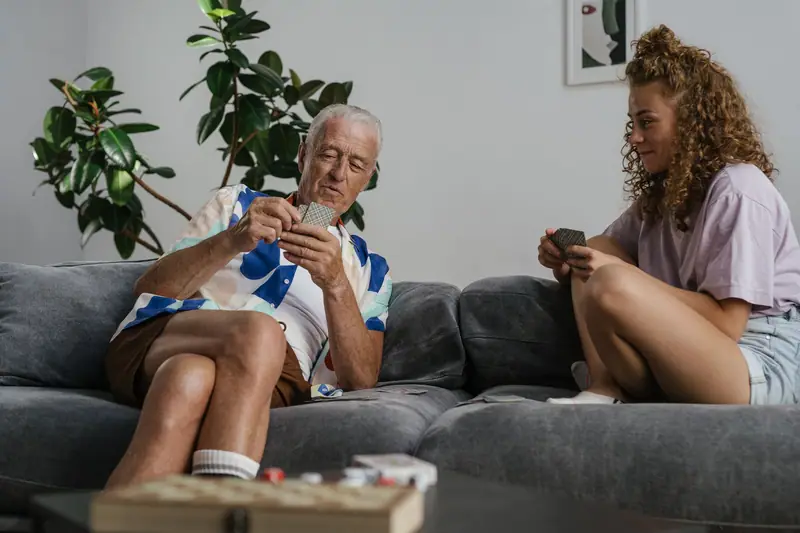 An older man playing cards with a younger woman on the sofa